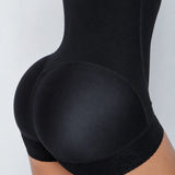 Close-up side view of a person wearing black shapewear shorts with a smooth front panel and sheer lace trim at the hip, shown against a light gray background.