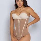 A woman modeling a strapless beige corset bodysuit with a structured bust, sheer mesh panels, vertical satin-like trim, and a front zipper, against a light gray studio background.