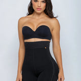 A woman modeling a black strapless bandeau-style top and high-waisted shapewear shorts set against a light gray studio background.