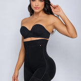 A woman modeling a black shapewear set consisting of a strapless bandeau-style bra and high-waisted briefs, photographed against a light gray studio background.