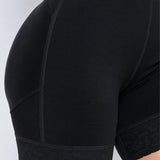 Close-up of black shapewear shorts with a lace hem, shown on a model against a light gray background.