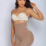 A woman modeling a beige high-waisted shapewear brief and a matching strapless bandeau bra against a light gray studio background.