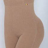Close-up side view of a person wearing high-waisted beige compression shorts or shapewear against a light gray background.