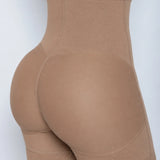Close-up of a model wearing high-waisted shapewear shorts in a solid taupe-brown color, shown from a side-rear angle against a light gray background.