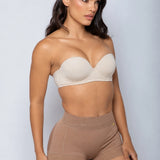 A woman modeling a beige strapless bra and matching high-waisted shorts against a light gray studio background.