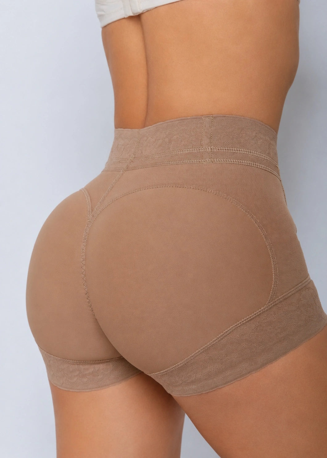 Rear view of a model wearing high-waisted shapewear shorts in a warm taupe-brown color, showing the seamless hip and butt contouring panels.