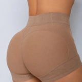 Rear view of a model wearing high-waisted shapewear shorts in a warm taupe-brown color, showing the seamless hip and butt contouring panels.
